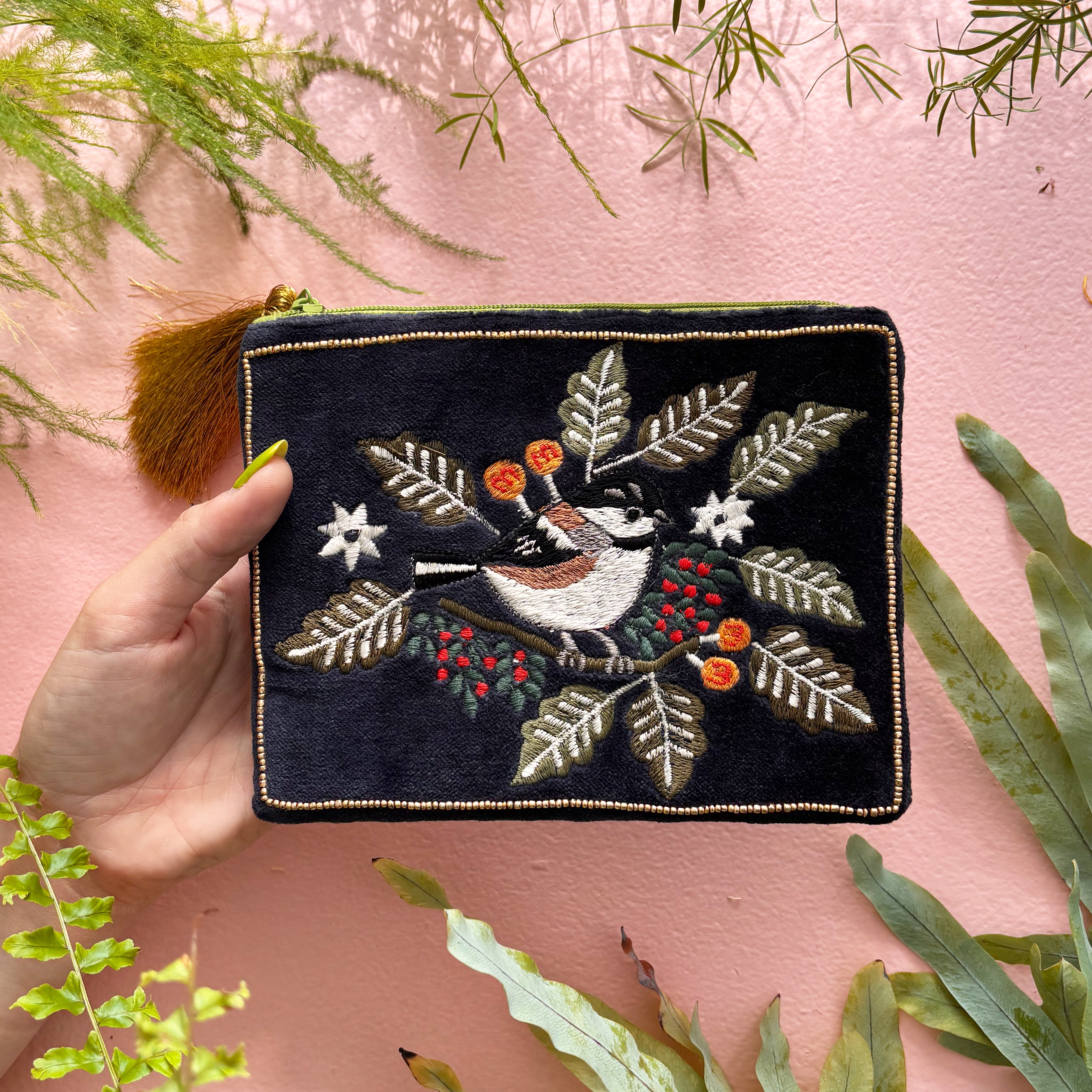 Navy velvet bird pouch held in hand showing embroidered front on pink background