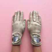 Beige embroidered hedgehog gloves worn on hands against pink background