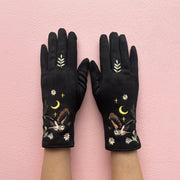 Black embroidered owl gloves worn on both hands against pink background
