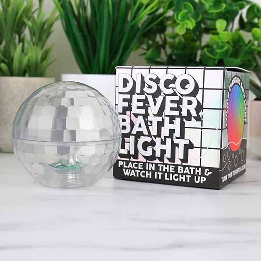 Clear disco-ball-shaped bath light beside its Disco Fever Bath Light packaging on a white countertop with plants in the background.