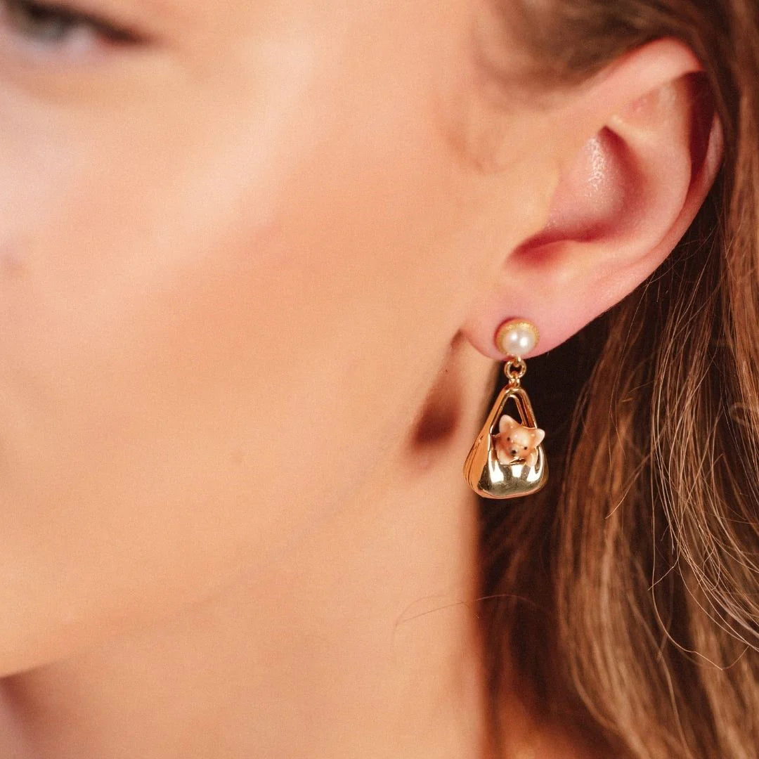 Close-up of Dog in a Bag Drop Earring worn on ear, showing pearl stud and enamel dog charm.