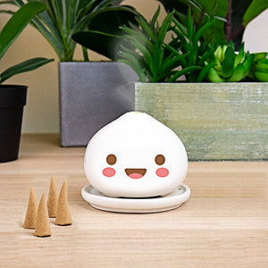 Cute ceramic dumpling incense burner on wooden table with plants and jasmine incense cones.