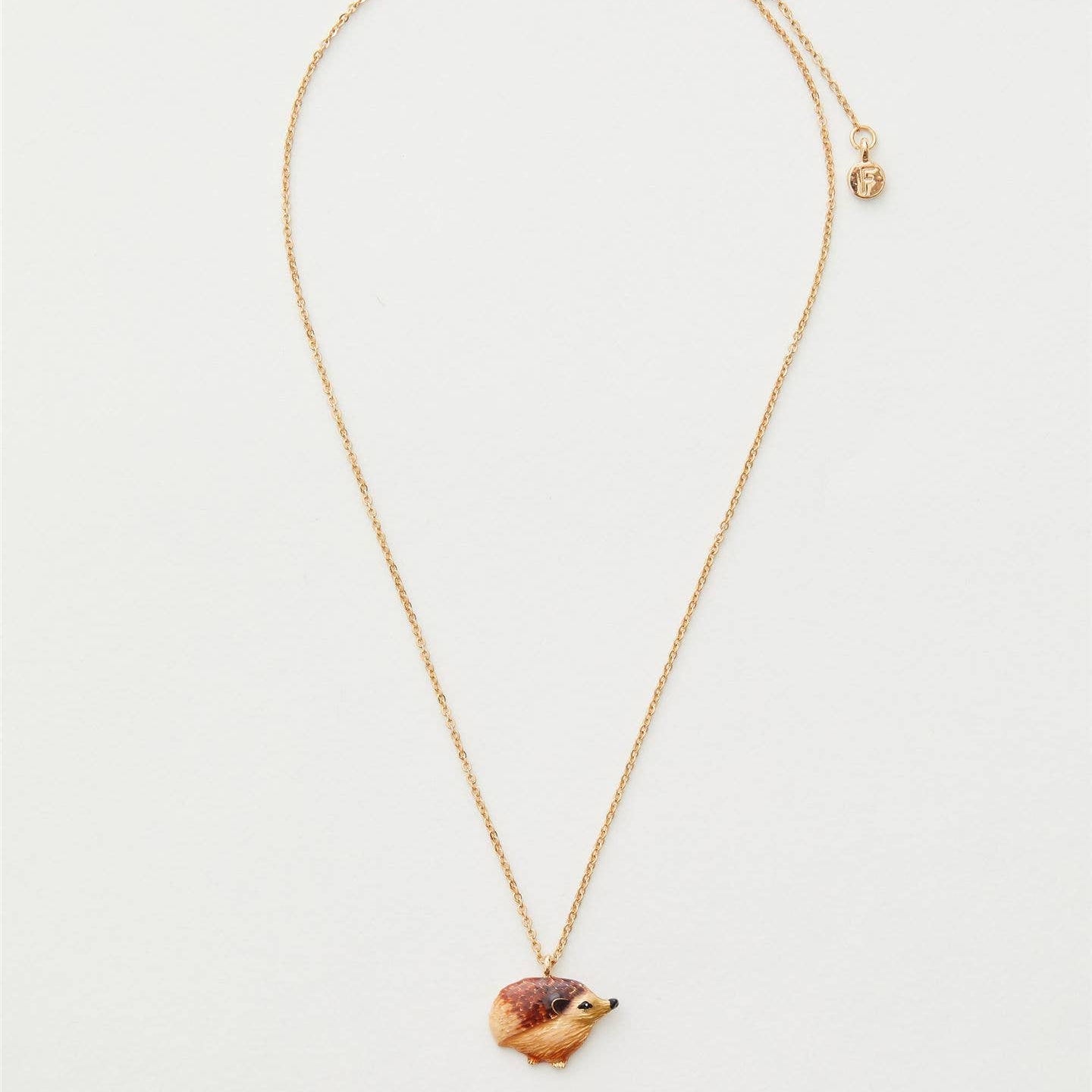 Enamel hedgehog necklace showing full gold chain length on cream background