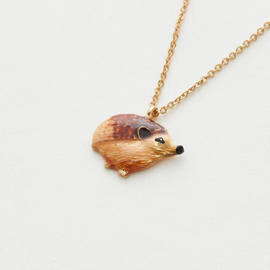 Enamel hedgehog pendant hanging on gold-plated chain against cream background