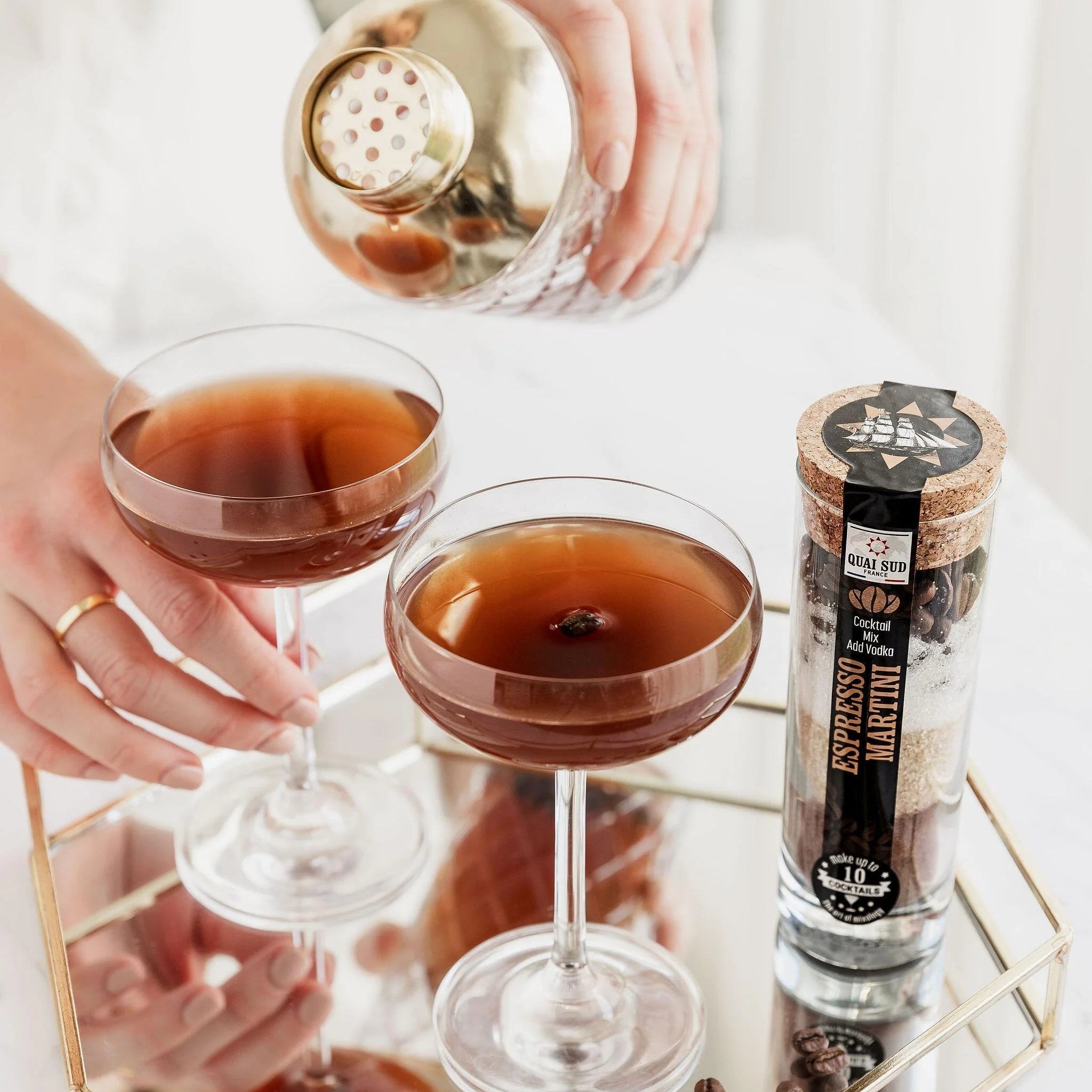 Two espresso martinis served on mirrored tray beside mix jar.