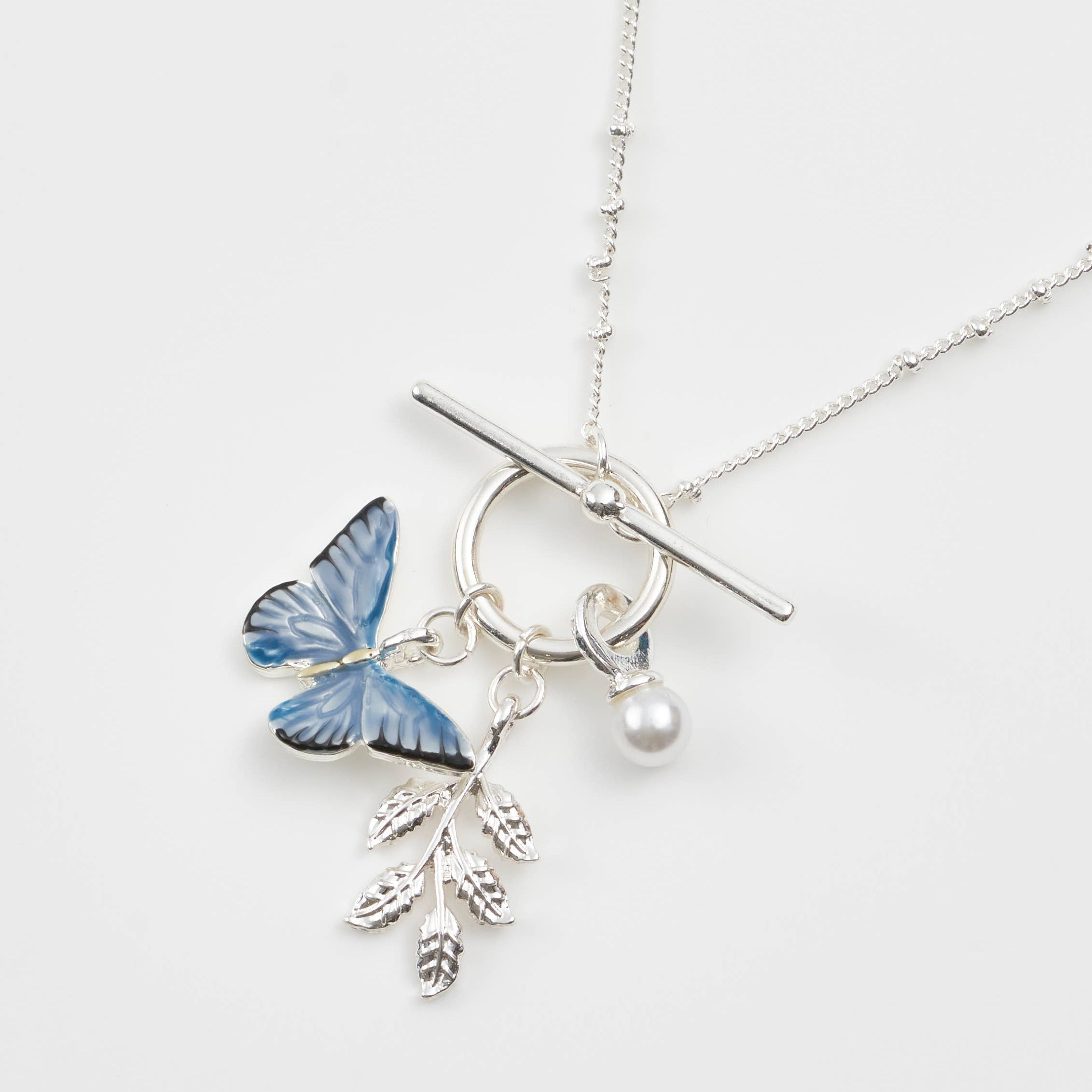 Blue butterfly T-bar necklace with pearl and leaf charms on white