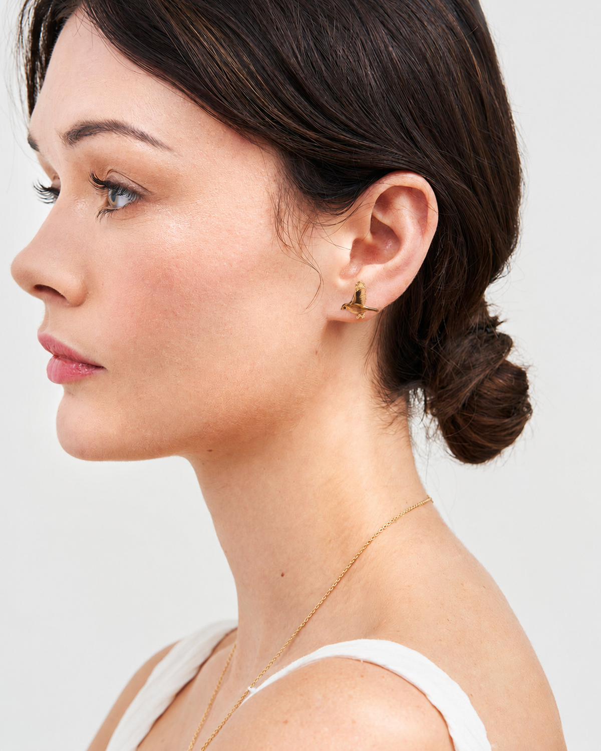 Flying robin stud earring worn by dark-haired model in profile
