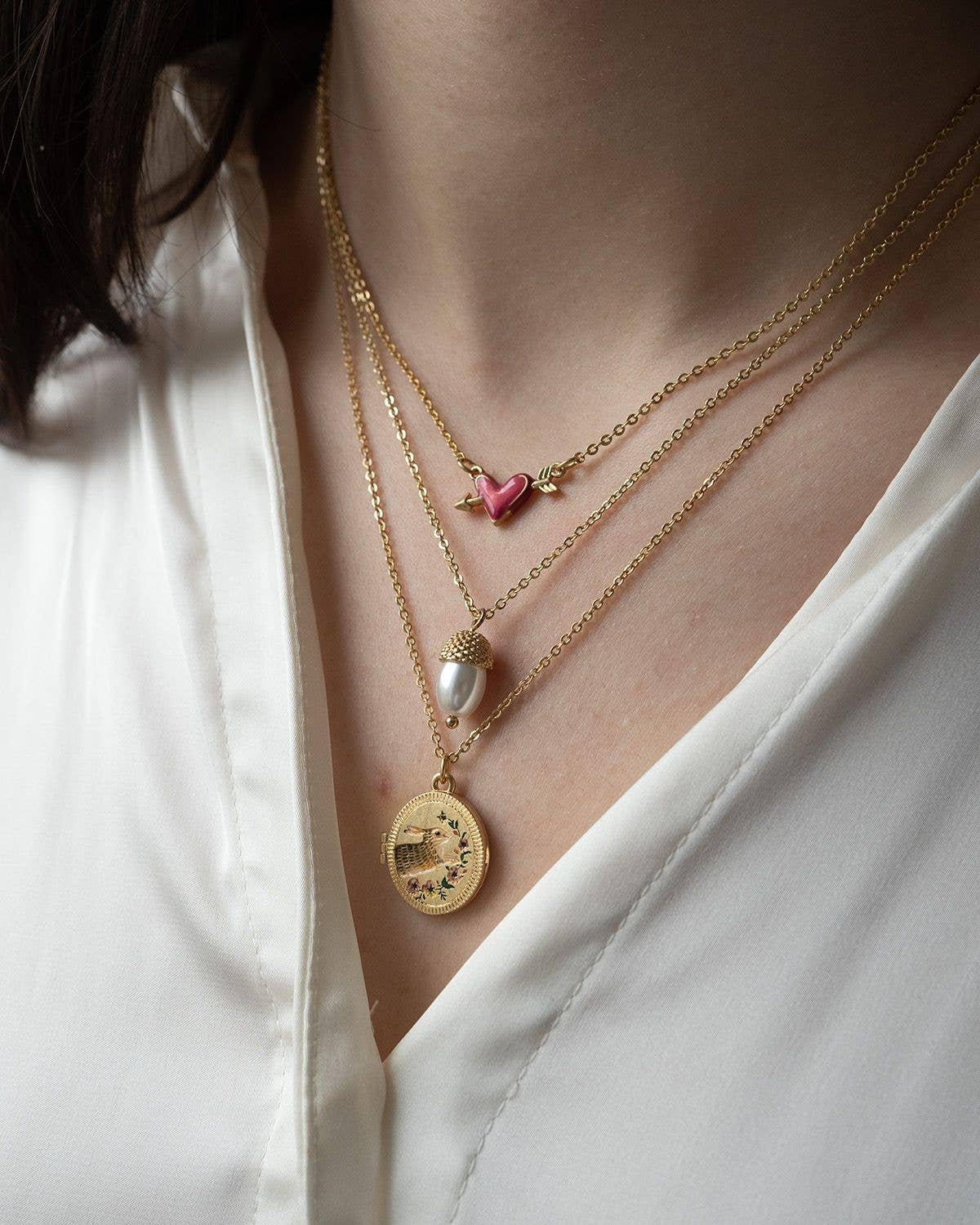 Running bunny locket worn layered with gold necklaces on white blouse