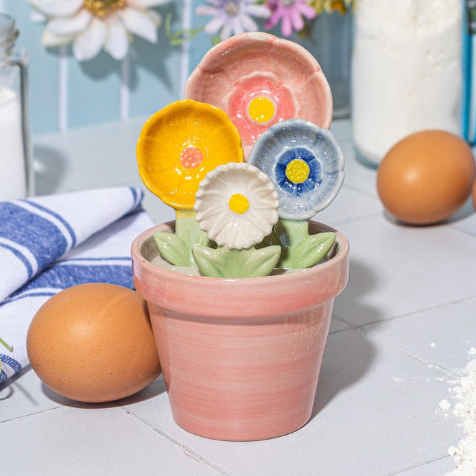 Ceramic flower measuring spoons displayed in terracotta pot with baking ingredients