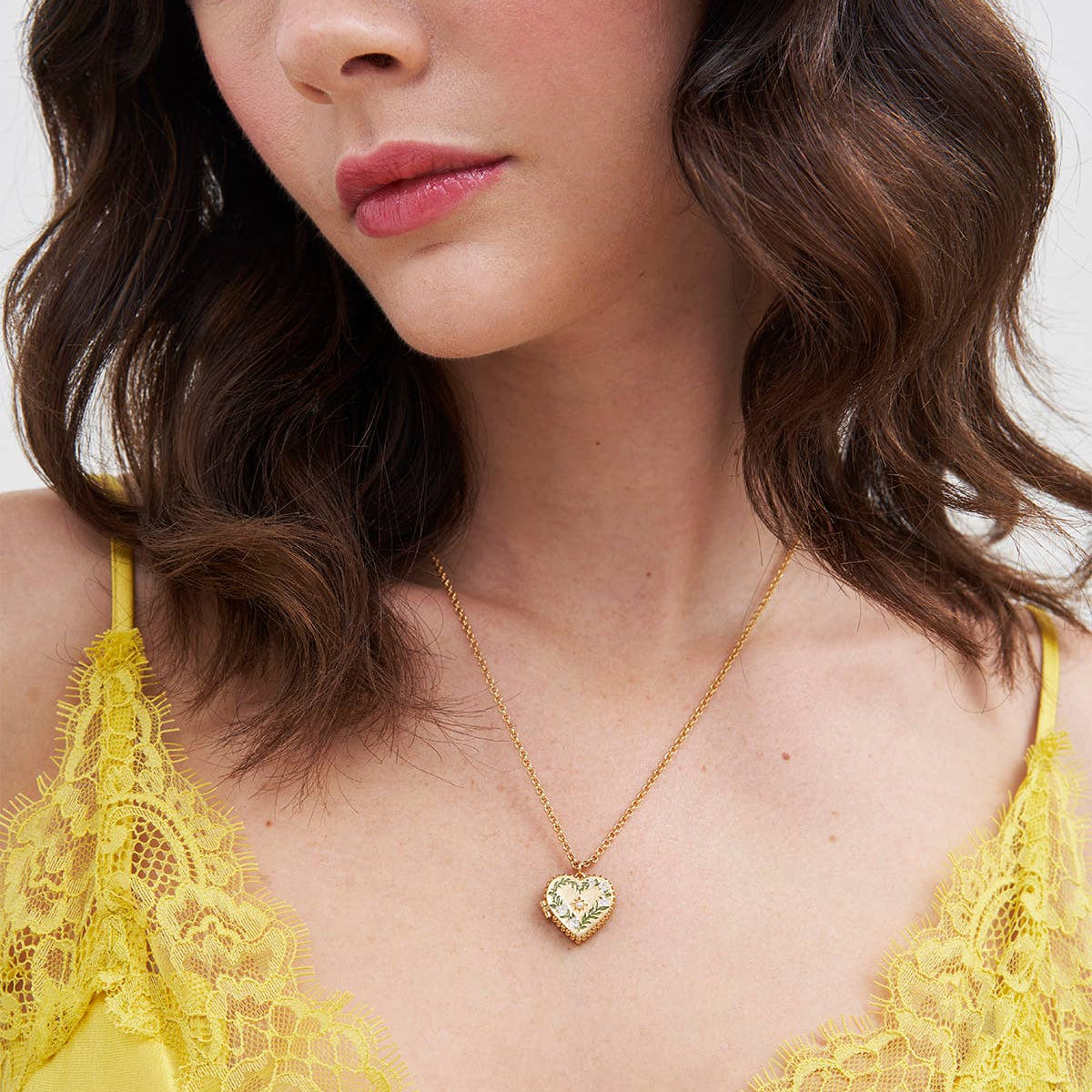 Model wearing Gaia Lily Heart Locket Necklace in gold with enamel lily detail.