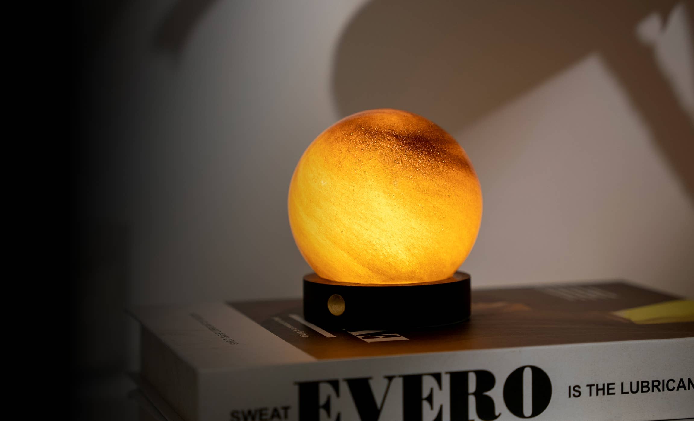 AstraGlass orb lit amber orange on black base against shadowed wall