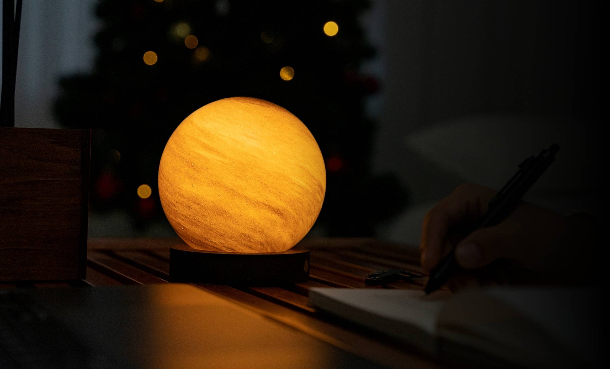AstraGlass orb glowing deep amber in a dark room with tree lights