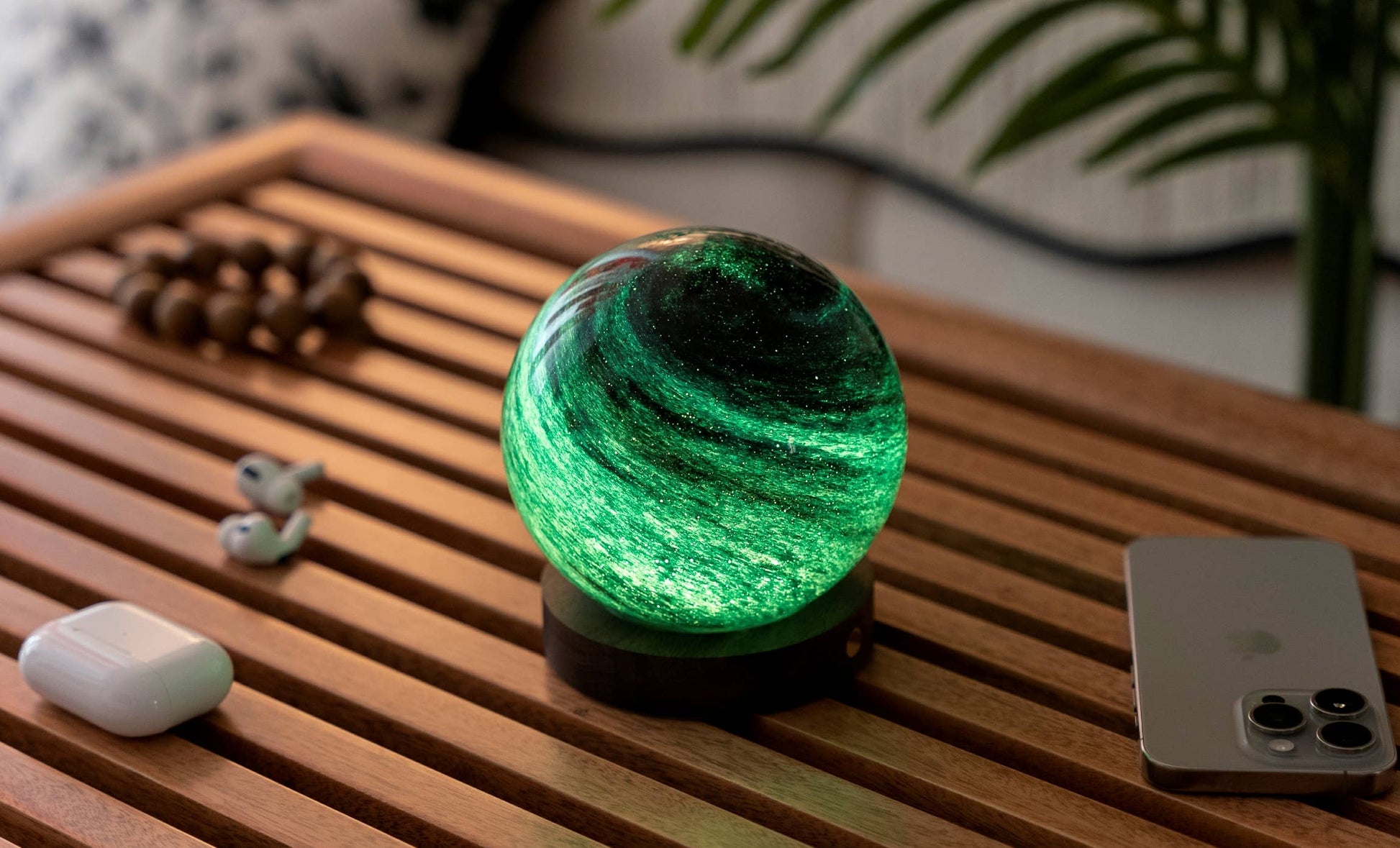 AstraGlass light glowing emerald green on coffee table with AirPods