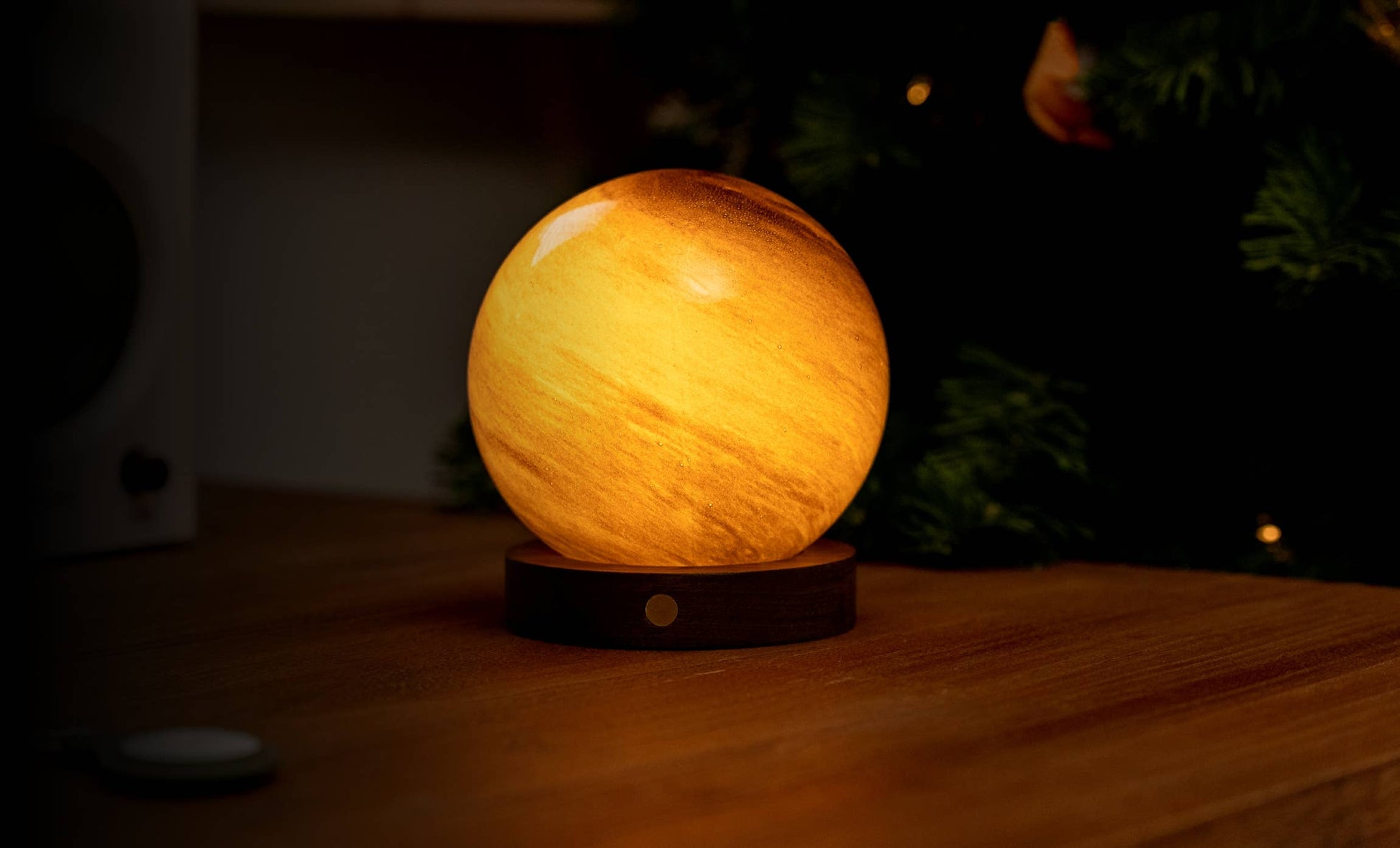 AstraGlass orb glowing golden amber on walnut base near Christmas tree