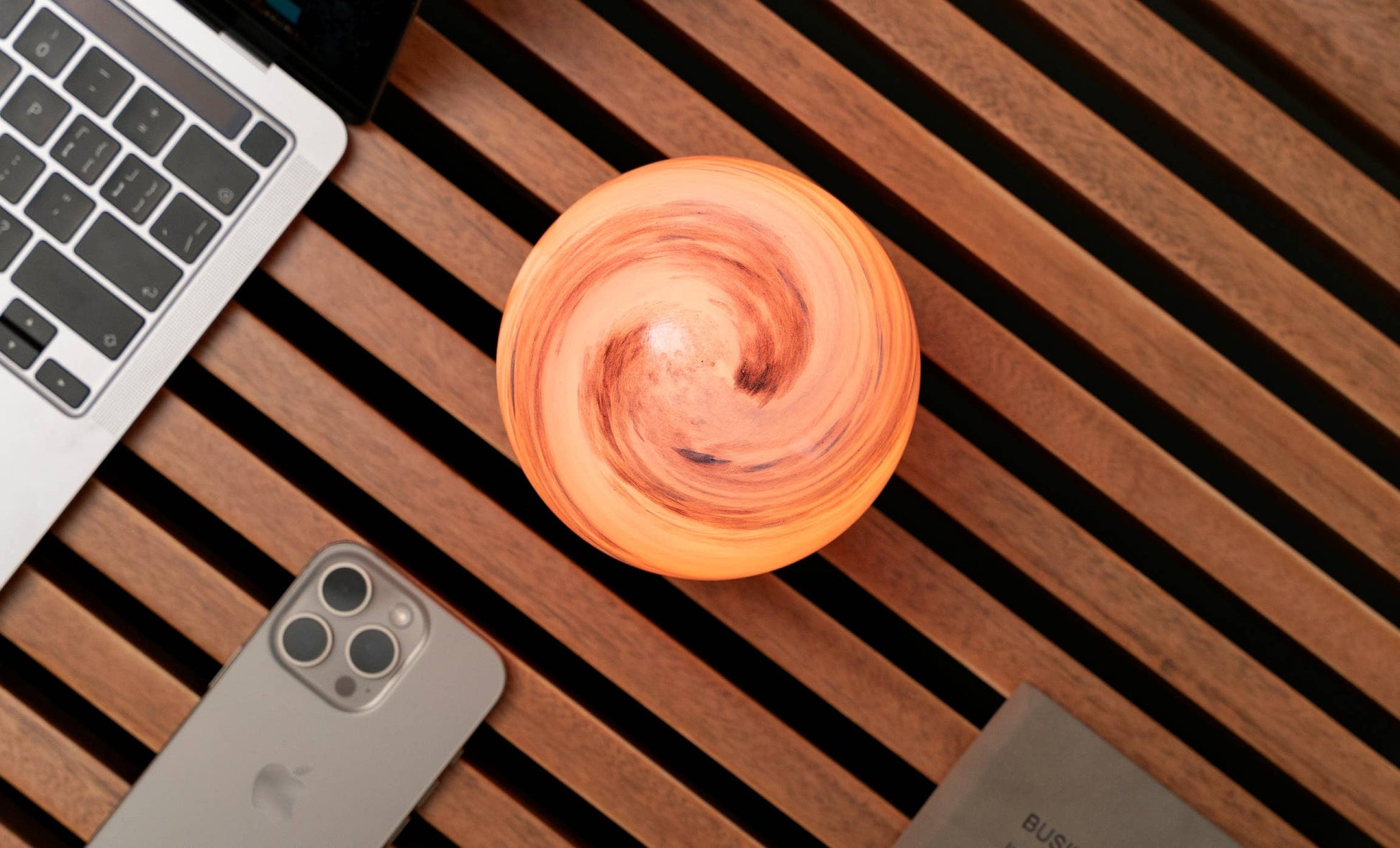 AstraGlass orb from above glowing soft orange swirl beside laptop