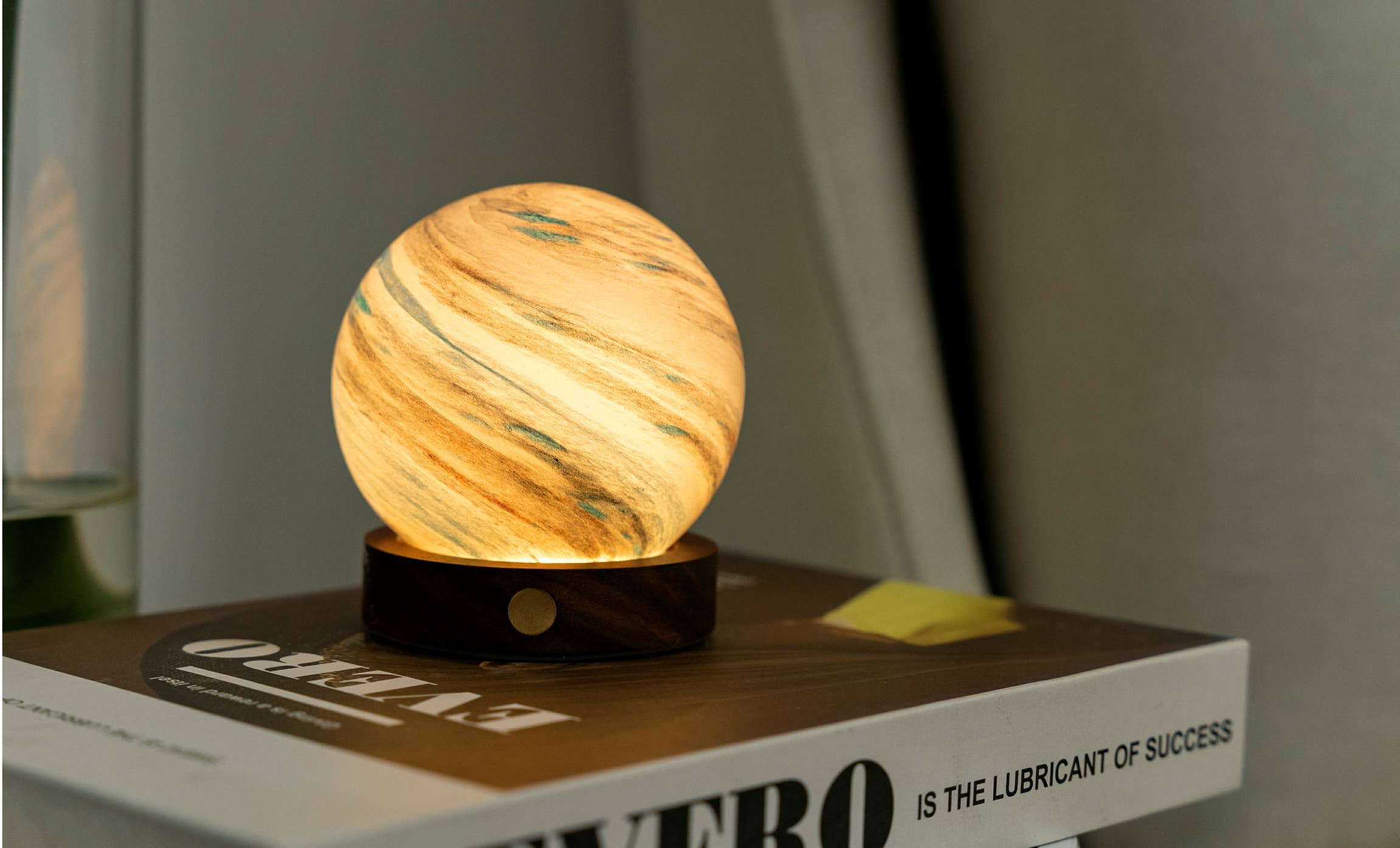 AstraGlass mini lamp glowing warm with teal streaks on stacked books