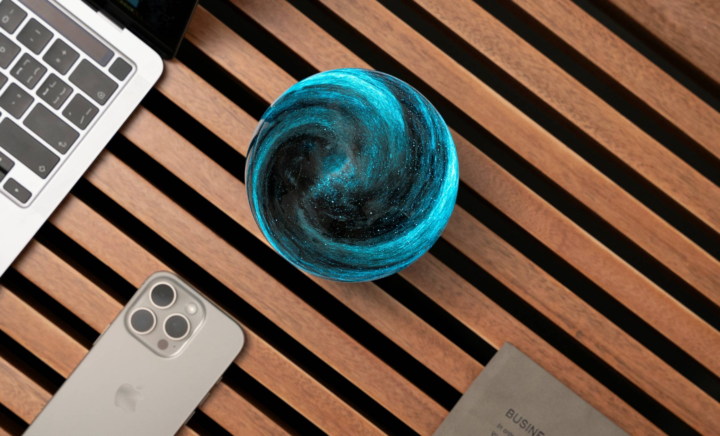 AstraGlass orb overhead view swirling teal and black beside phone