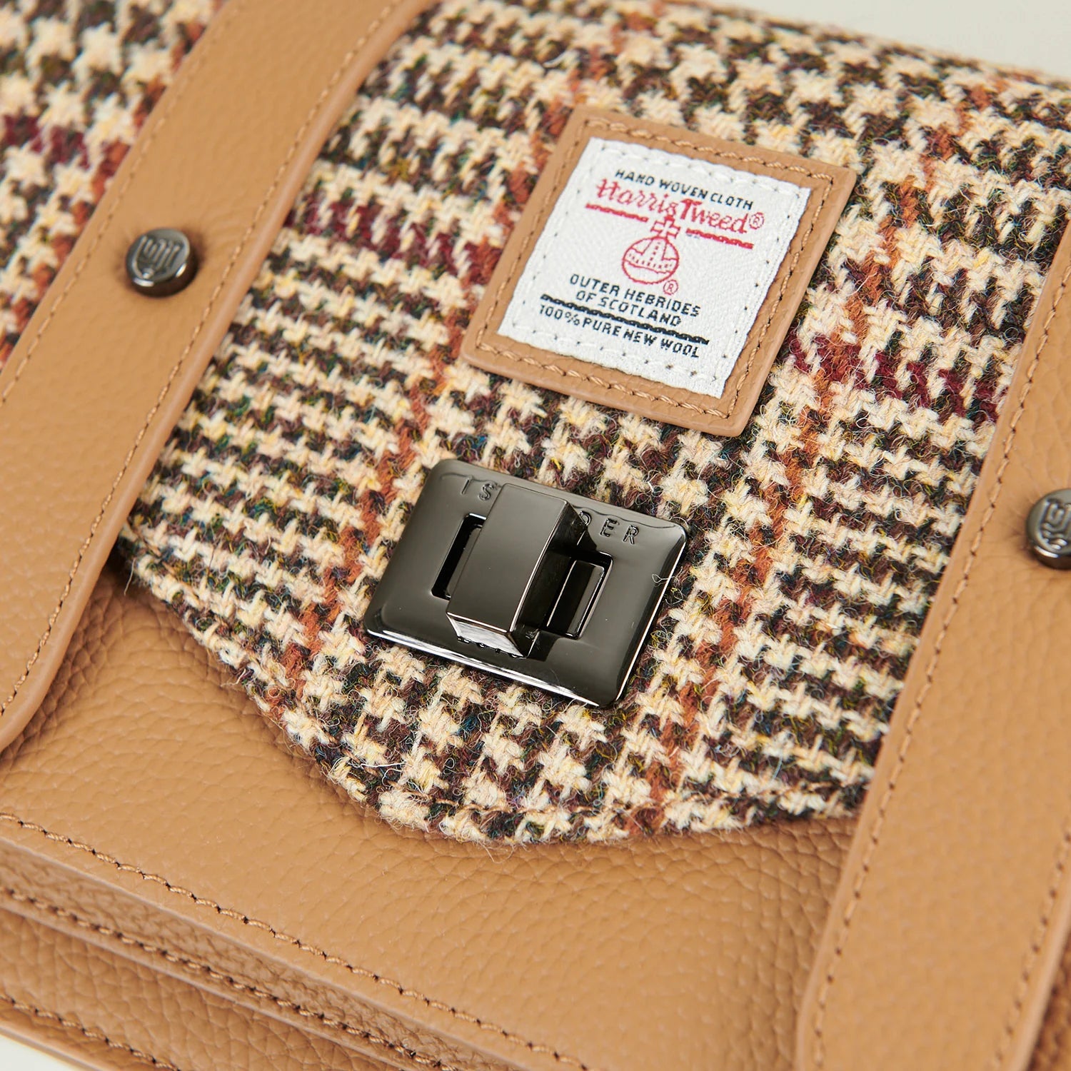 Harris Tweed authenticity label and metal twist clasp on beige leather satchel.