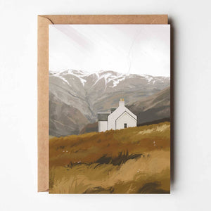 Highland House cosy cottage greeting card featuring illustrated white cottage against Scottish mountains, paired with kraft envelope.