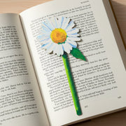 Painted daisy flower bookmark lying on open book on wooden surface