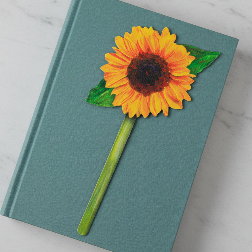 Painted sunflower bookmark on closed teal book on marble surface