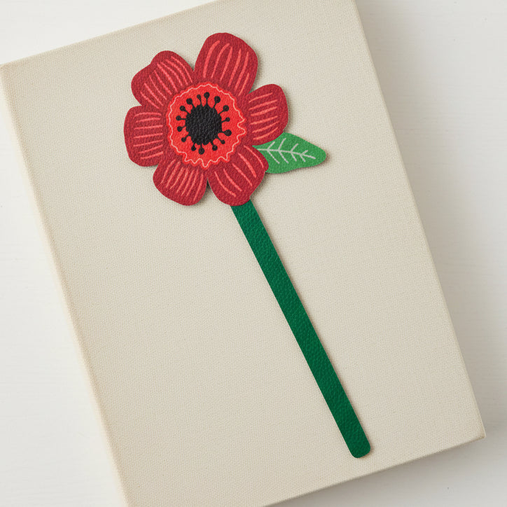 Red poppy flower bookmark on closed cream book grey background