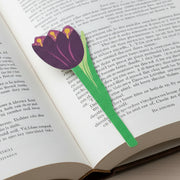 Purple tulip flower bookmark on open book on wooden surface