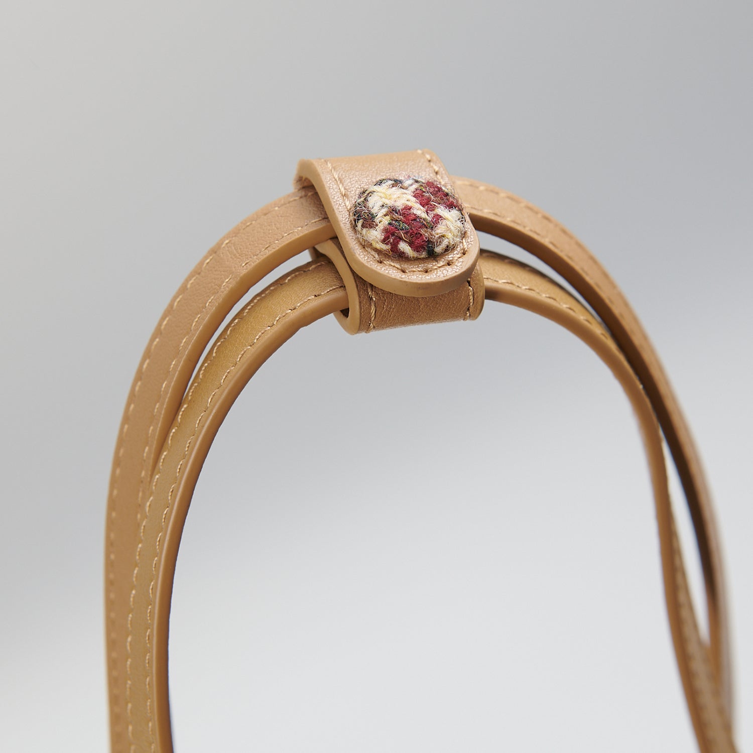 Close-up of leather handle button detail on beige dogtooth bucket bag