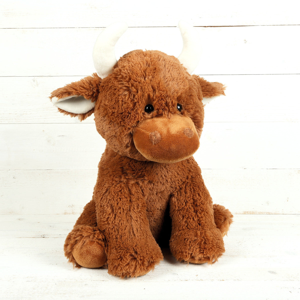 Brown Highland cow plush toy front view on white wooden background