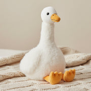 Cream goose soft toy sitting on knitted blanket with beige background