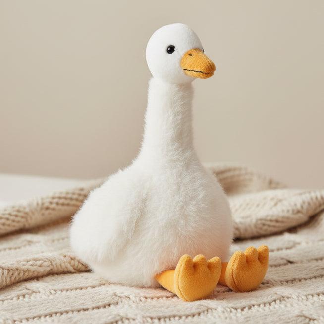 Cream goose soft toy sitting on knitted blanket with beige background
