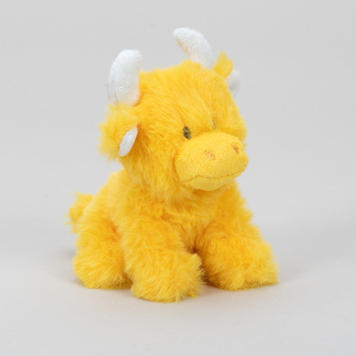 Mini orange Highland cow soft toy side view with white horns on grey background