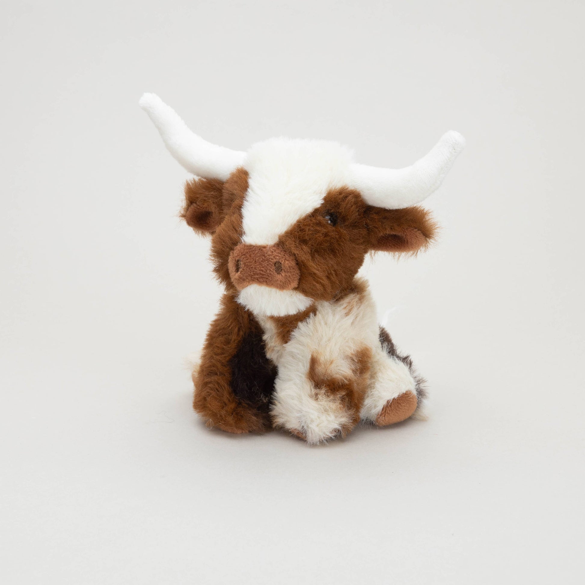 Texas Longhorn mini soft toy cow sitting with white horns on grey background