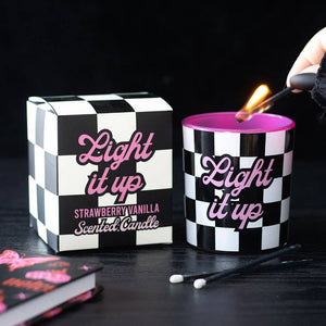 Light It Up Strawberry Vanilla Candle with black and white checkerboard design and pink lettering, lit beside matching gift box.