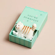 Striped ceramic cat token in open mint green matchbox on beige surface