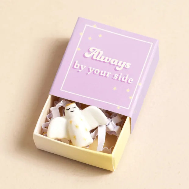 Ceramic angel nestled inside open lilac matchbox on cream background