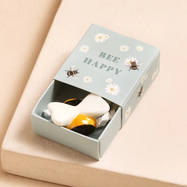 Ceramic bee inside open sage green matchbox with daisy and bee design on cream background