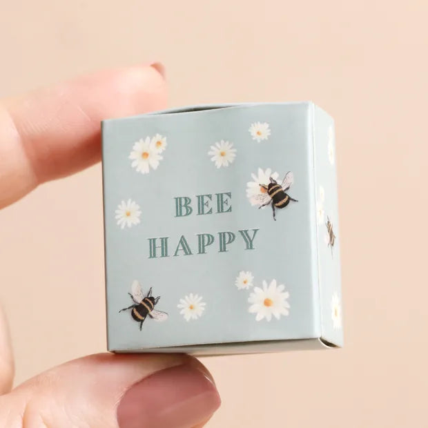 Hand holding closed sage green matchbox with bee and daisy print on cream background