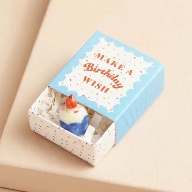 Ceramic cupcake inside open confetti matchbox with blue lid on cream background