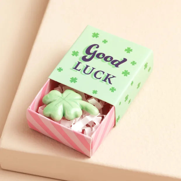Green ceramic clover inside open matchbox with mint green lid on cream background