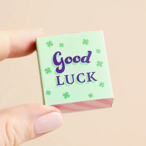 Hand holding closed mint green matchbox with clover print on cream background