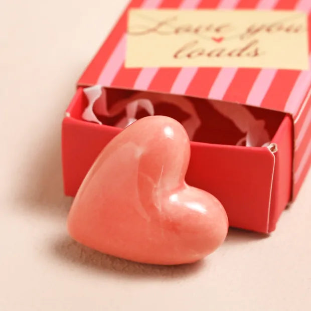 Pink ceramic heart token beside open red-striped matchbox on cream background