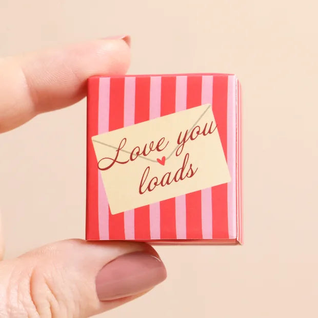 Hand holding closed red and pink striped matchbox with envelope design on cream background
