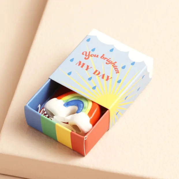 Ceramic rainbow inside open blue matchbox with sunshine and raindrop design on cream background
