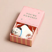 White ceramic dog token in open pink matchbox on beige surface