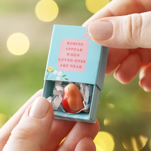 Ceramic robin token held in open blue matchbox with green bokeh background