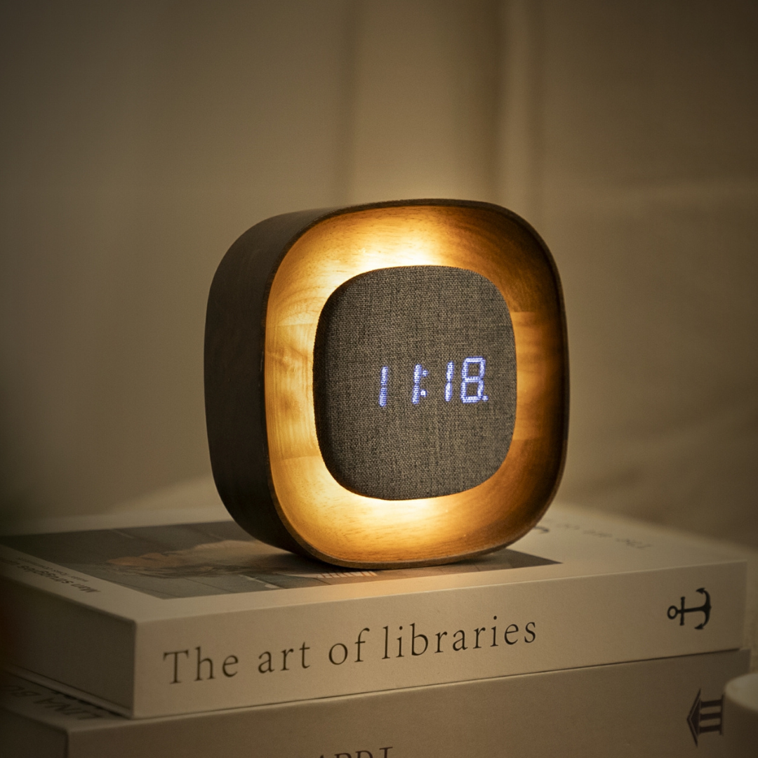 Square walnut Lumos clock glowing on stacked books
