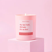 My Last Fuck candle in a matte pink jar, lit against a pale pink backdrop
