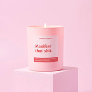 Manifest That Shit positivity candle in matte pink jar lit on a pink backdrop