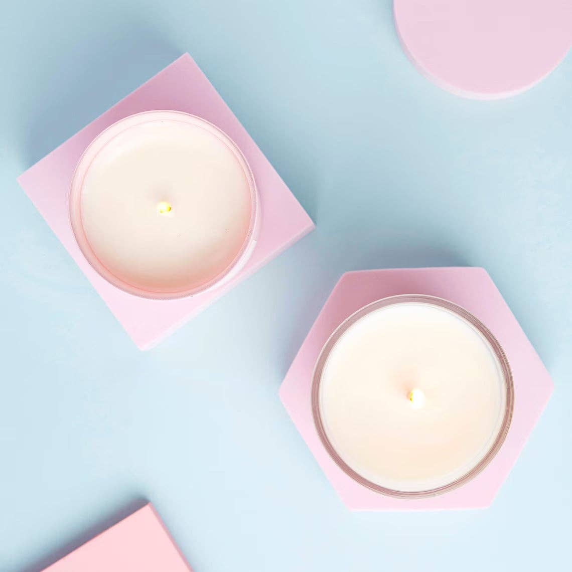 Positivity candles viewed from above, lit in pink holders on a pale blue surface